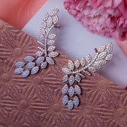 A pair of silver earcuffs designed to resemble an olive branch, displayed on a textured pink background with a flower for scale.